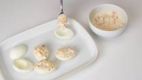 Abre los huevos duros a lo largo y retira las yemas. Mezcla las yemas con 2 cucharadas de bechamel y trabaja hasta formar una pasta espesa. Cubre los huevos con esta masa y déjalos enfriar.