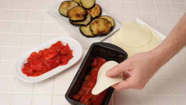 Corta a tiras los pimientos asados. Engrasa un molde de pastel y alterna en capas las rodajas de berenjena, pimiento y lonchas de queso sin llenar el molde.
