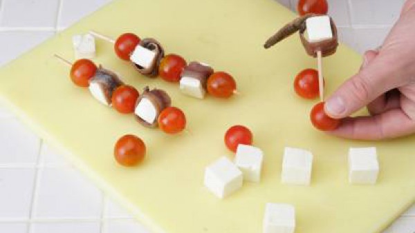 Inserta un tomate y un taco de queso con una anchoa a su alrededor y tepite la operación tantas veces como sea necesario. Se finaliza la brocheta con otro tomate Cherry.