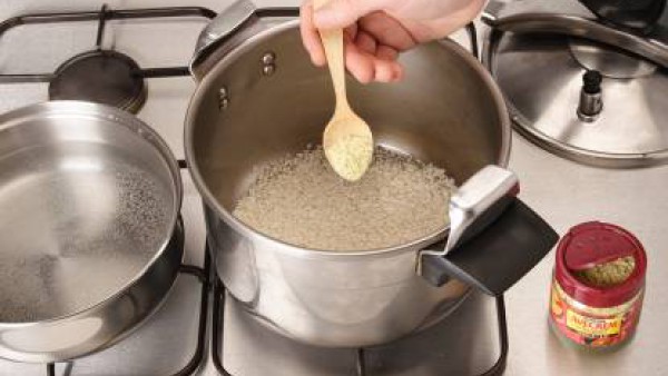 Pon un poquito de aceite en la olla rápida, rehoga el arroz con el sazonador Avecrem. Riega con el agua caliente.