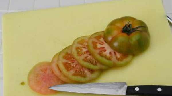 Corta el tomate por la mitad en sentido perpendicular. Presiona para quitarle las semillas, sala un poco y deja invertido para que se escurra. Luego calienta el aceite en una sartén, echa el tomate co