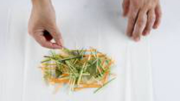 Corta las verduras en tiritas finas. Corta el limón en rodajas y los ajos en láminas finas. Pon las verduras y las hierbas frescas sobre una hoja de papel de horno.