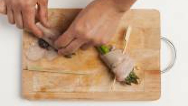 Después de la cocción, dispón los filetes de pechuga de pollo en una tabla de cortar y rellénalos con el paté de aceitunas y los espárragos. Enróllalos y ciérralos con un pincho.